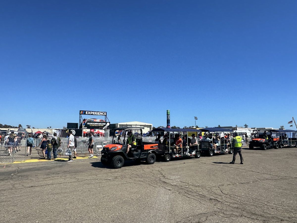 FlexTram trams loaded with fans at a NASCAR event with parking staff directing traffic