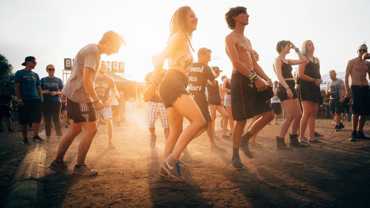 A crowd of festival-goers dancing in dusty golden-hour light at an outdoor music festival