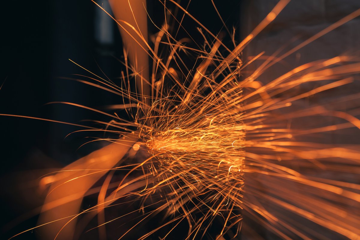 Bright orange sparks scattering against a dark industrial background, evoking friction and lost energy