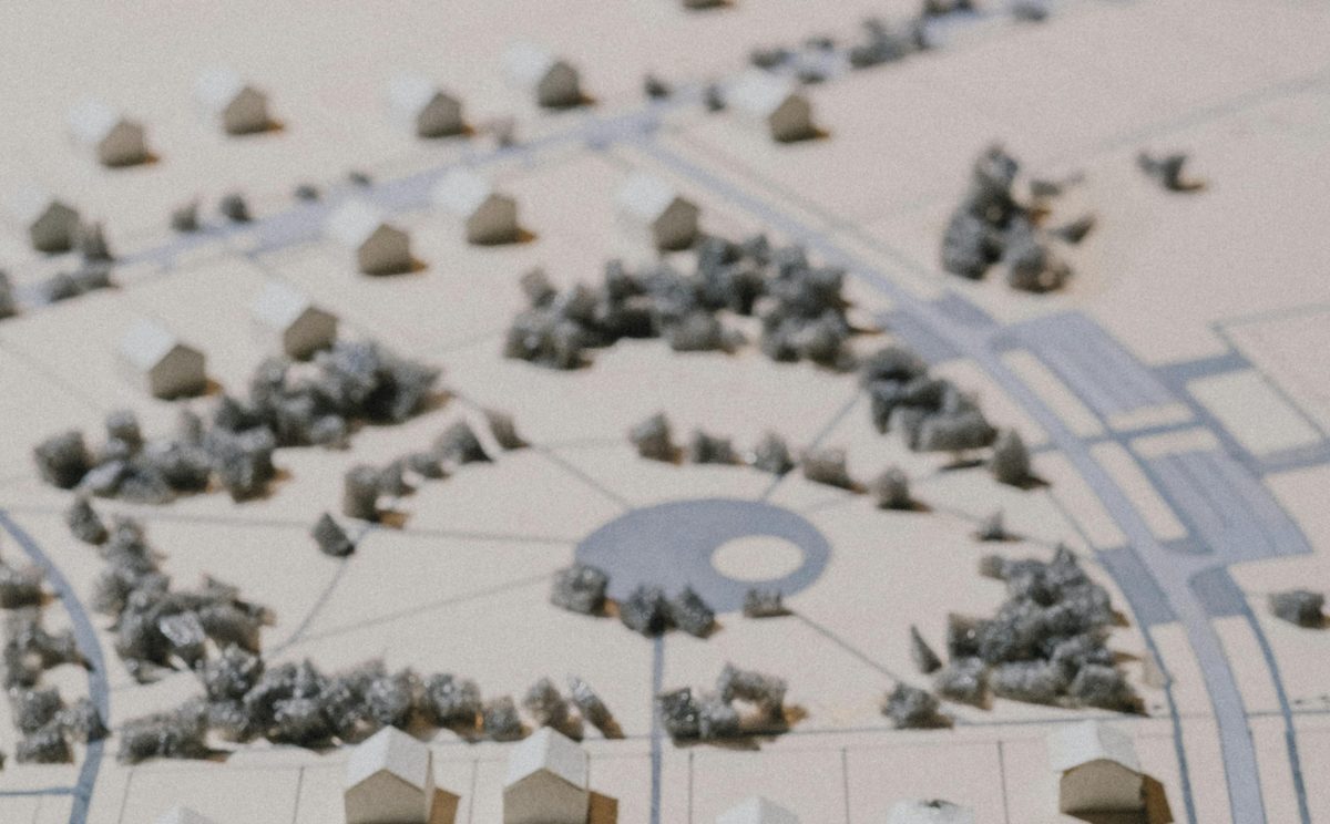 Architectural campus model of a planned senior living community showing a central plaza, curving paths, model trees, and house pieces arranged across a designed footprint