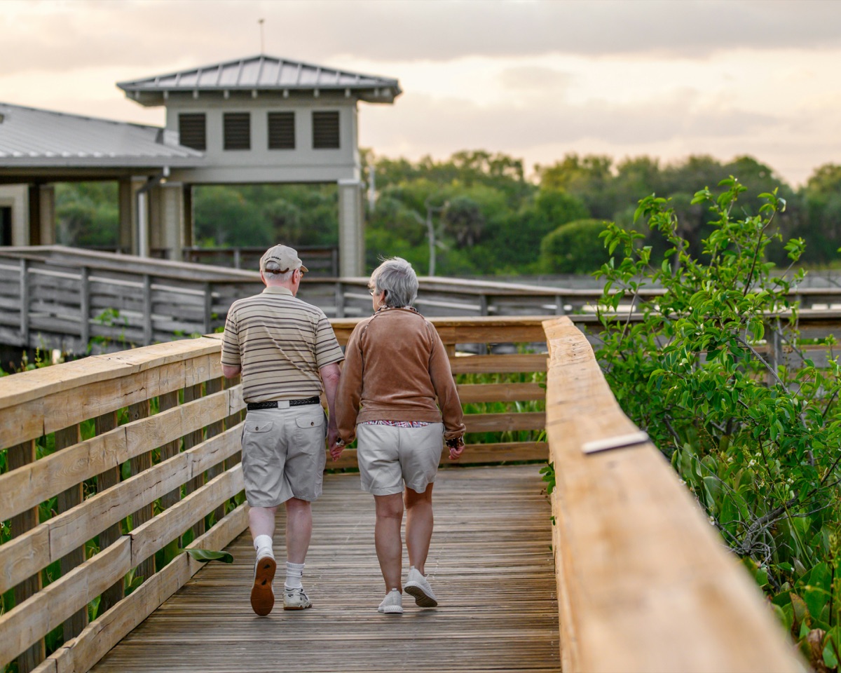Senior couple walking along boardwalk pathway at retirement community