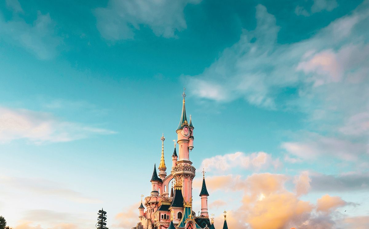 Disneyland Paris Sleeping Beauty Castle at sunset framed against a dramatic cloud-streaked sky, evoking the guest-facing magic that depends on invisible backstage logistics