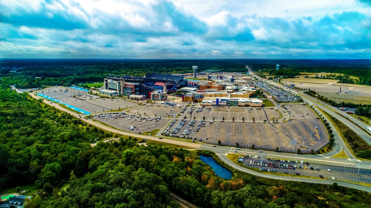 Aerial view of Gillette Stadium and Patriot Place in Foxborough surrounded by vast parking lots and forest, with Route 1 alongside