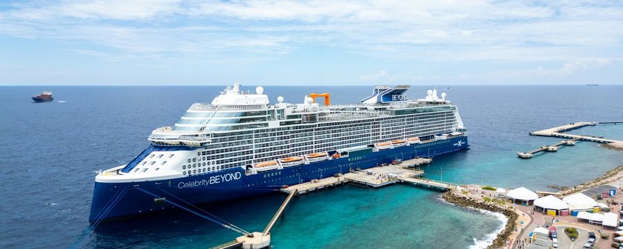 Celebrity Beyond cruise ship docked at a Caribbean port with turquoise water and colorful pavilions