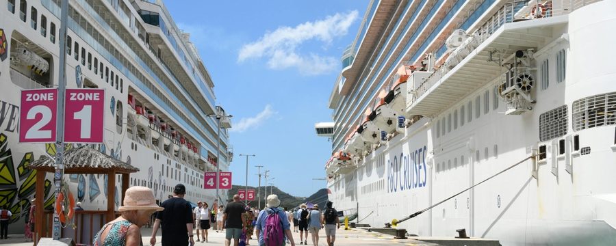 Cruise passengers walking along a pier between two docked cruise ships on turnaround day