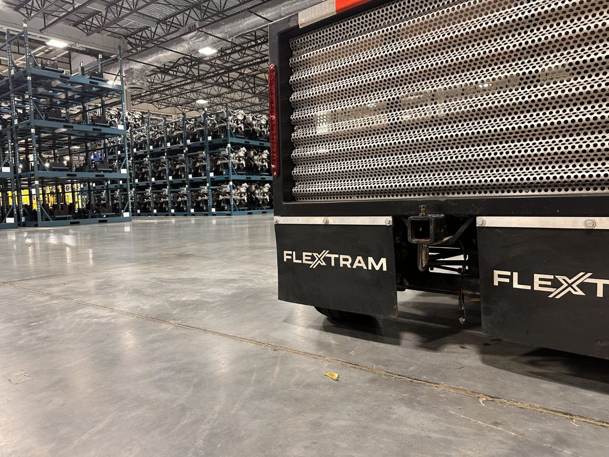 Rear of a FlexTram car with FLEXTRAM mud flaps, parked indoors beside racks of engines at a manufacturing plant
